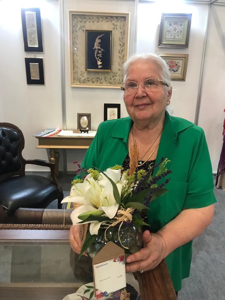 Seher Ayral, Craft İstanbul 2023 etkinliğinde geleneksel el sanatlarını sergilerken kendisine gelen çiçekle ile çekildiği fotoğraf karesi.